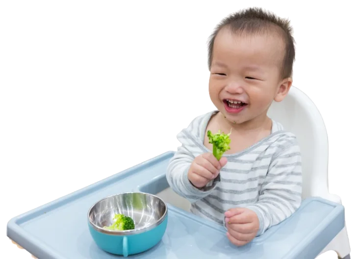 Smiling toddler in a high chair holding broccoli
